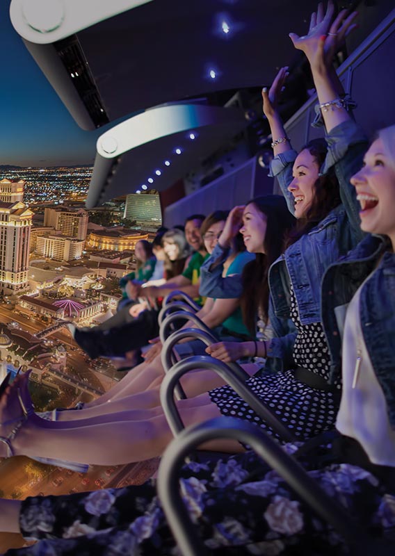 A group of people on a flight ride, superimposed over a view of the Las Vegas Strip